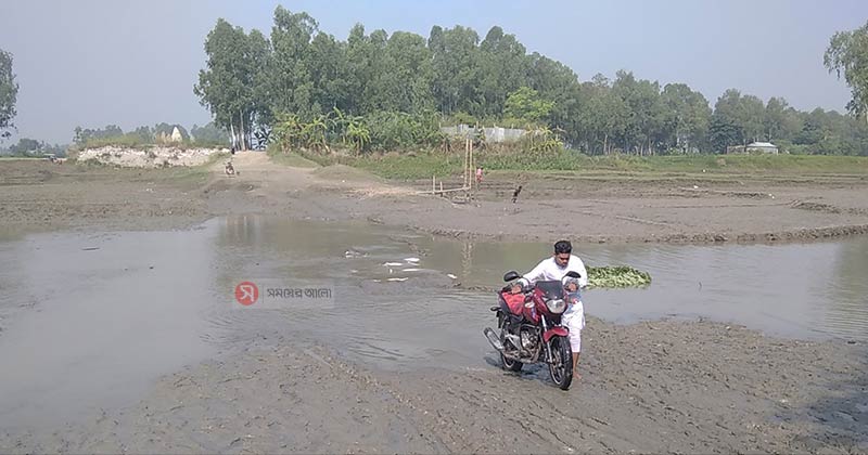 রাজীবপুর উপজেলা সদর ইউনিয়নের খাঁজার ঘাট এলাকায় কাদা পানিতে পারাপার হচ্ছেন মানুষ । ছবি: সময়ের আলো